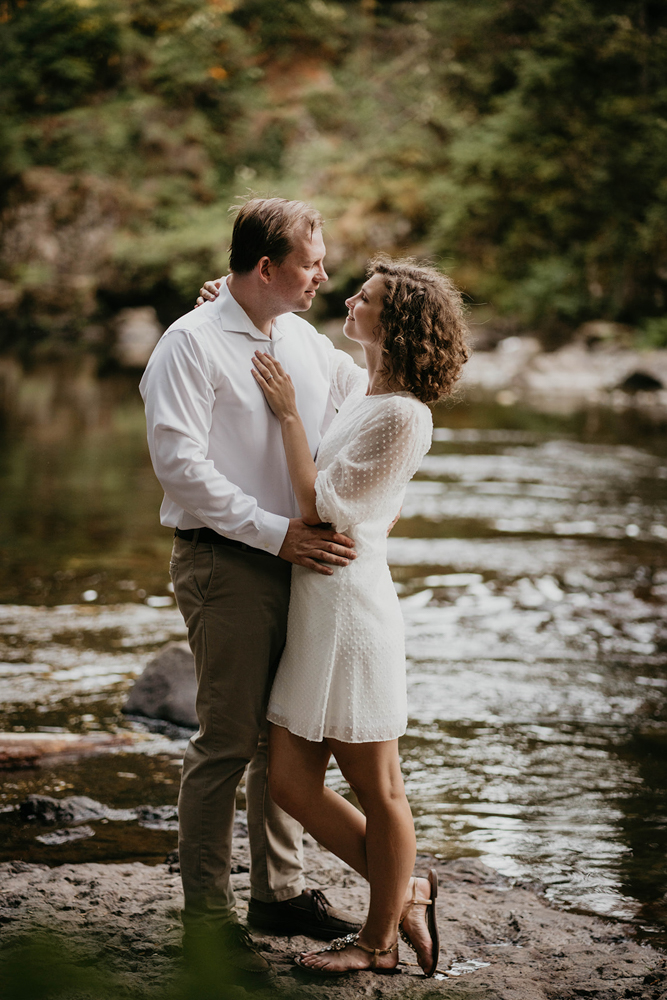 A couple staring lovingly into each other eyes as a river babbles behind them at Moulton Falls.