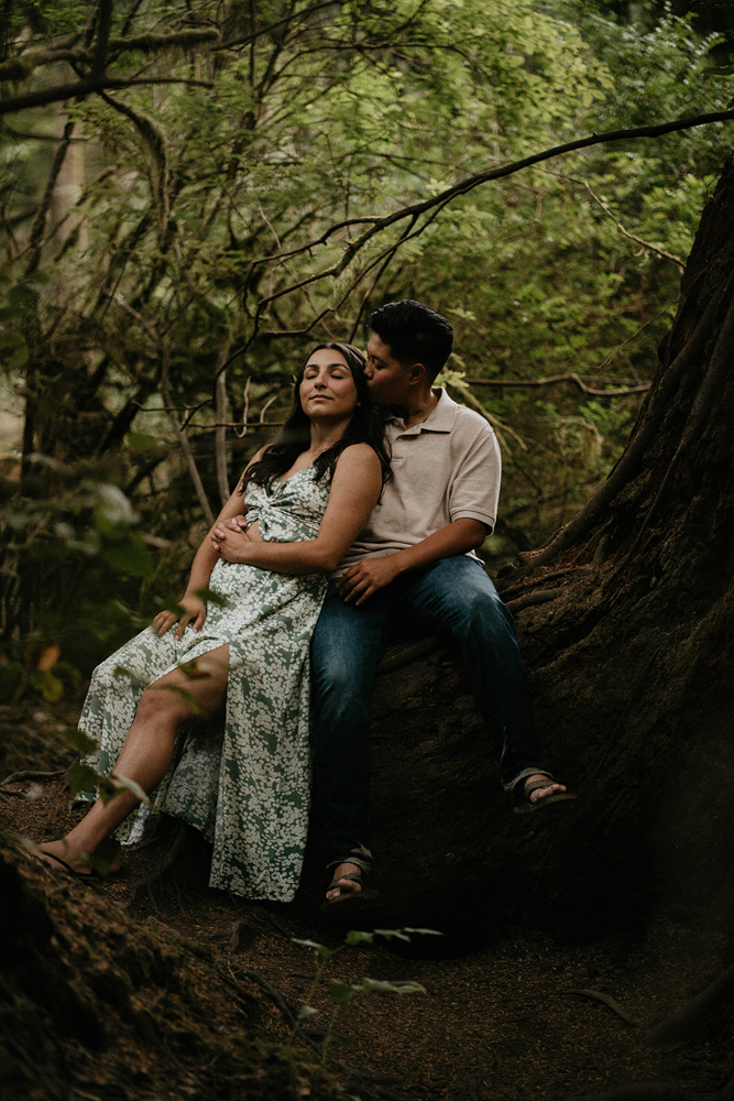 A couple sharing an intimate moment sitting on a tree with the forest in the background at Short Sand Beach. 