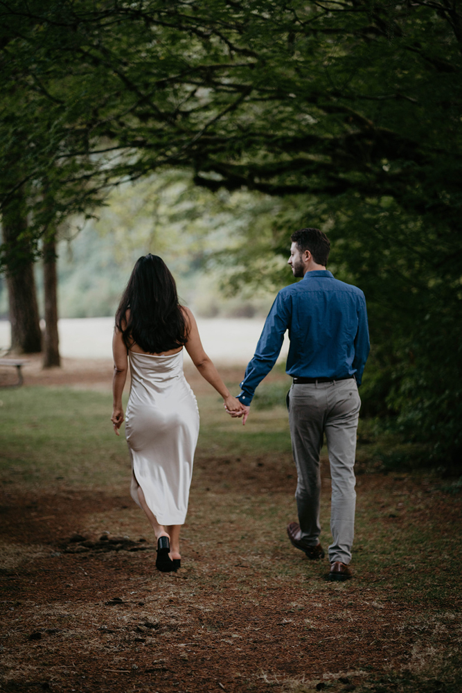 A couple holding hands while walking through a tunnel of trees at Silver Falls. 