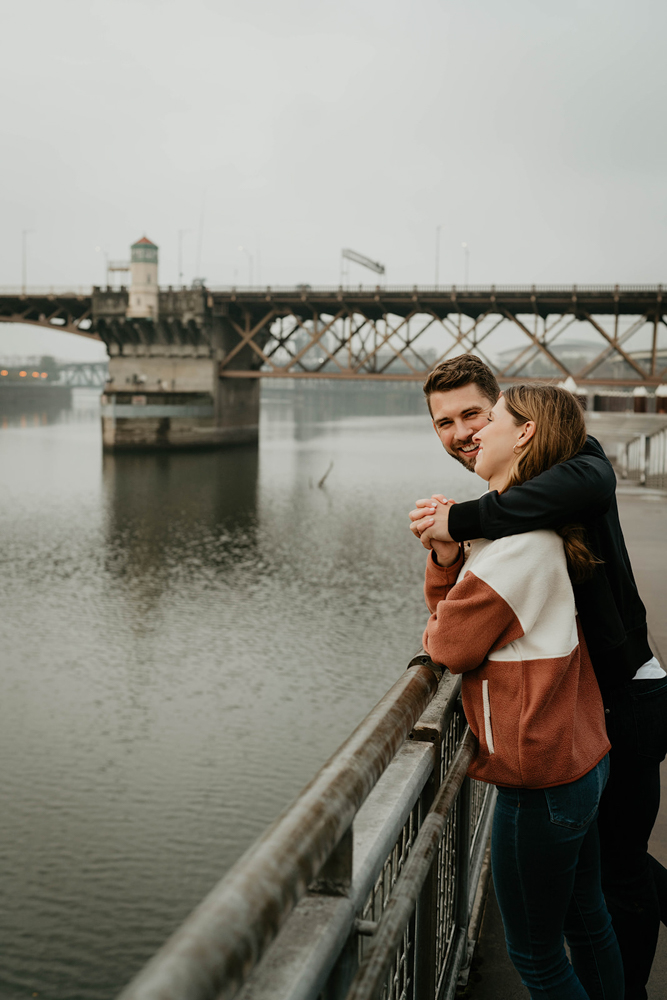 A couple kissing in front of a steal bridge along the Willamette River Waterfront in Portland. 