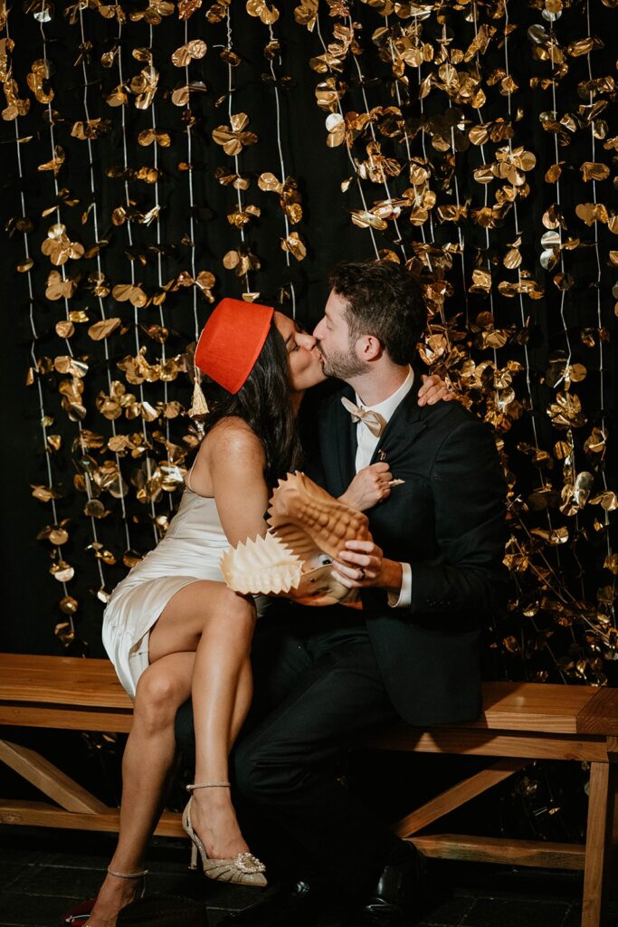 Bride and groom kiss while holding and wearing props at their Blockhouse Portland wedding