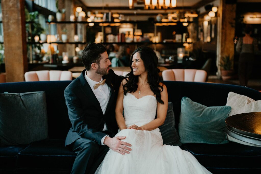 Bride and groom sit on a blue velvet couch for wedding portraits at their Blockhouse wedding in Portland