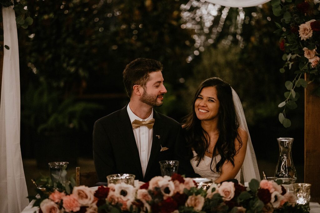 Bride and groom sit at head reception table during their Blockhouse wedding in Portland