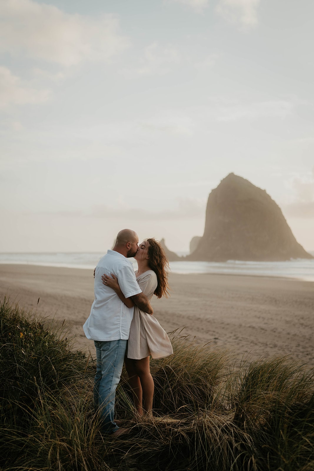 Couple kisses in the grassy sand dunes during their Cannon Beach Oregon Coast engagement photo session