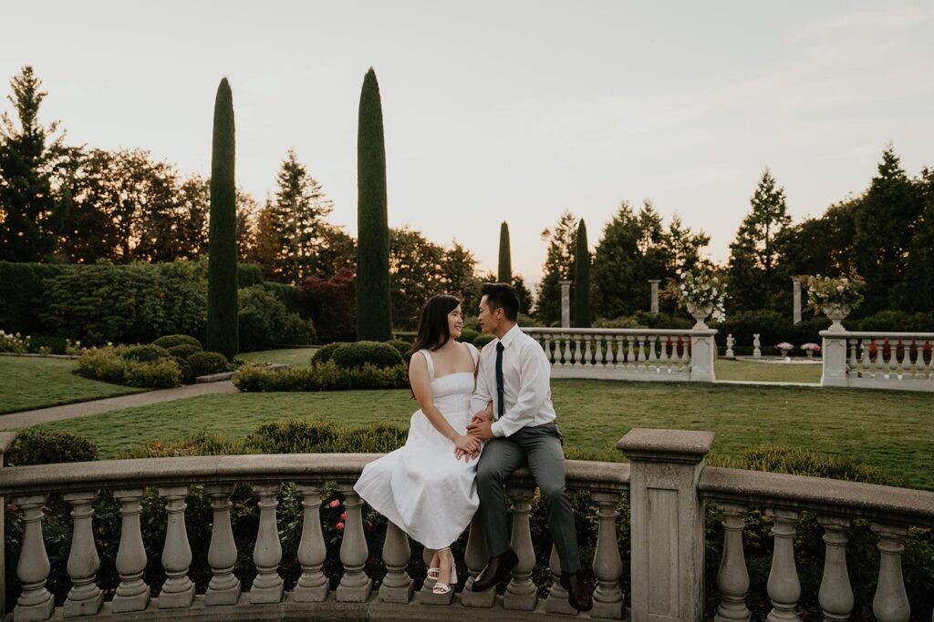 Couple sits on a garden ledge during their Oregon engagement photo session at Chateau de Michellia