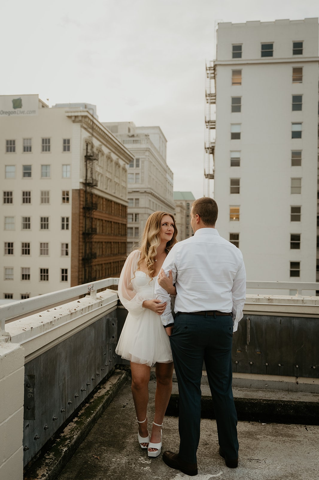 Couple links arms during their Oregon engagement photo session on a roof in downtown Portland