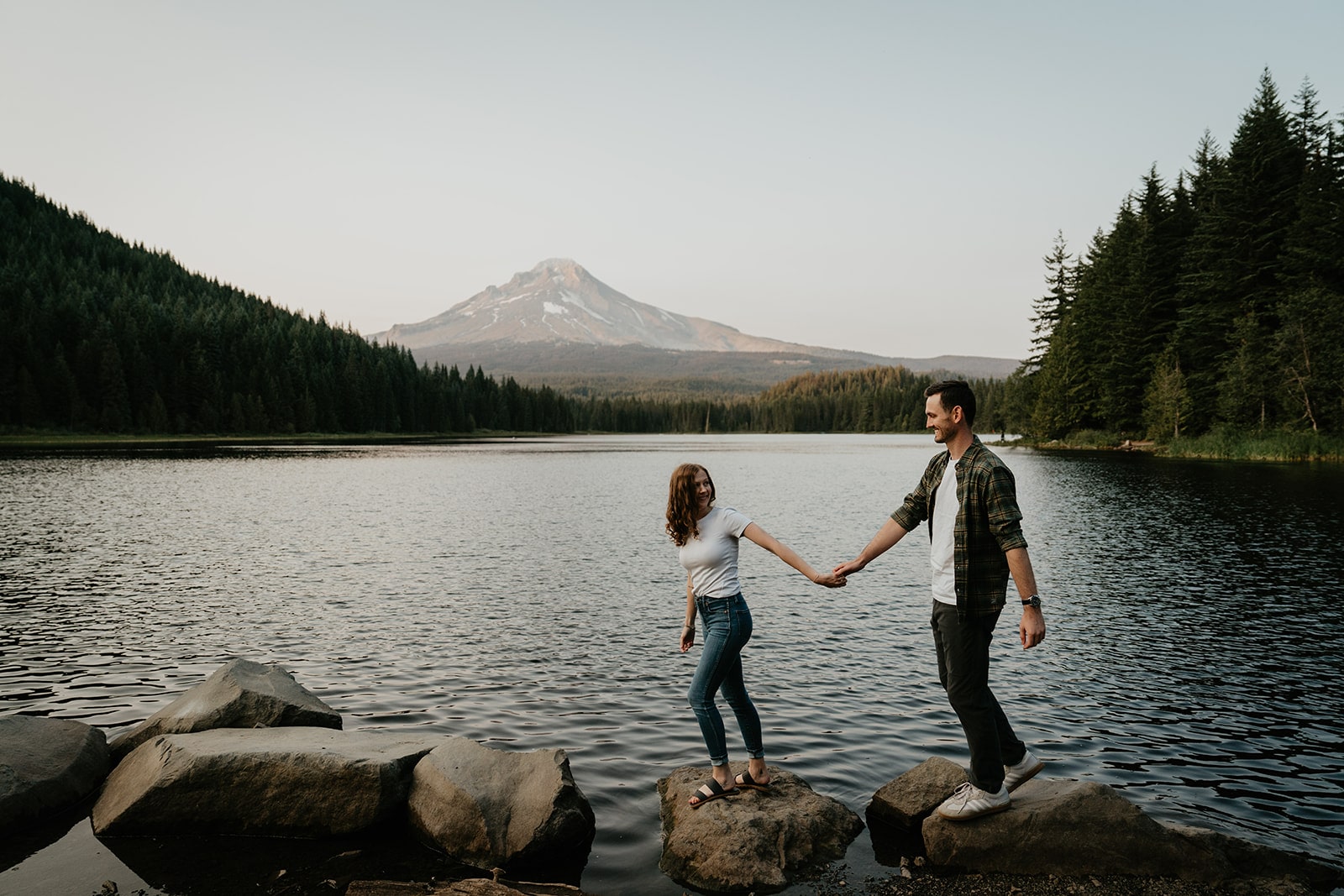 Couple holds hands while walking across the rocks during their Oregon engagement photo session