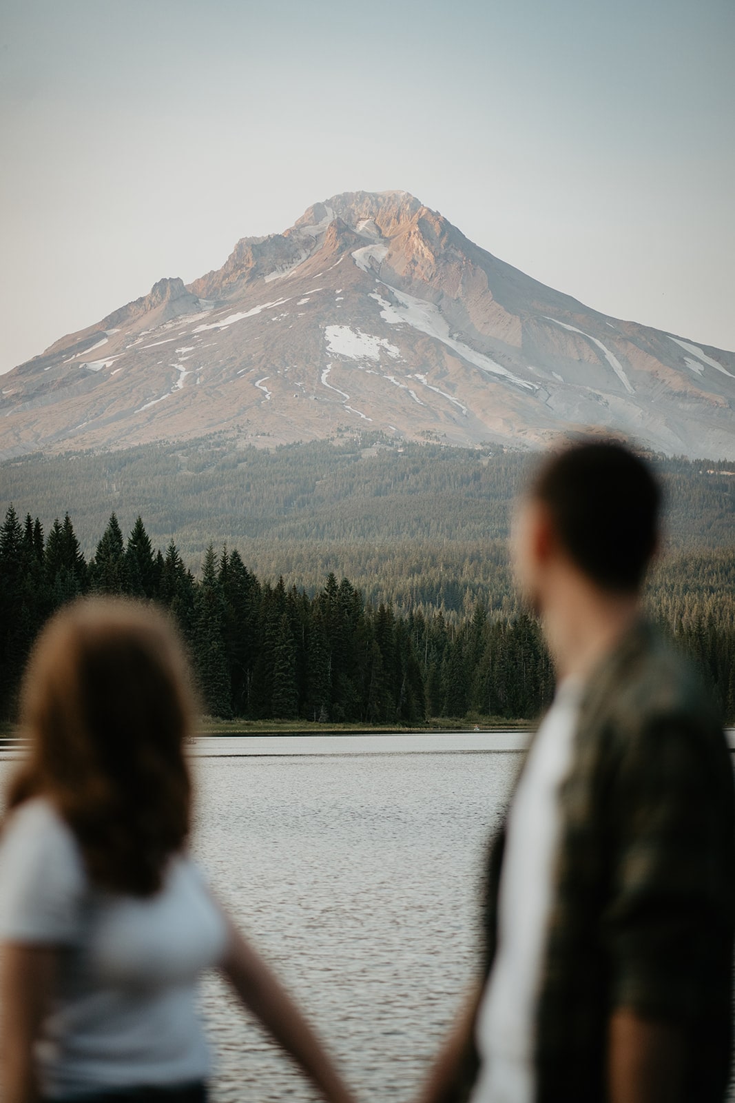 Couple holds hands while looking out across Lake Trillium at Mt Hood during their Oregon engagement photo session