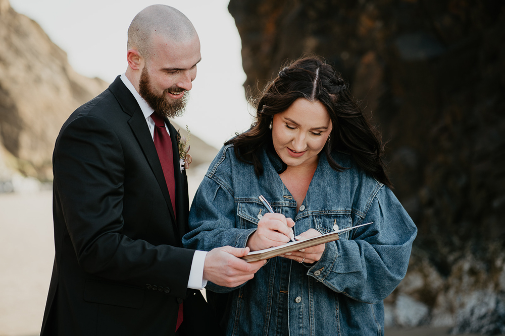 The newlyweds signing their marriage papers with sea stacks in the background at Cannon Beach. 