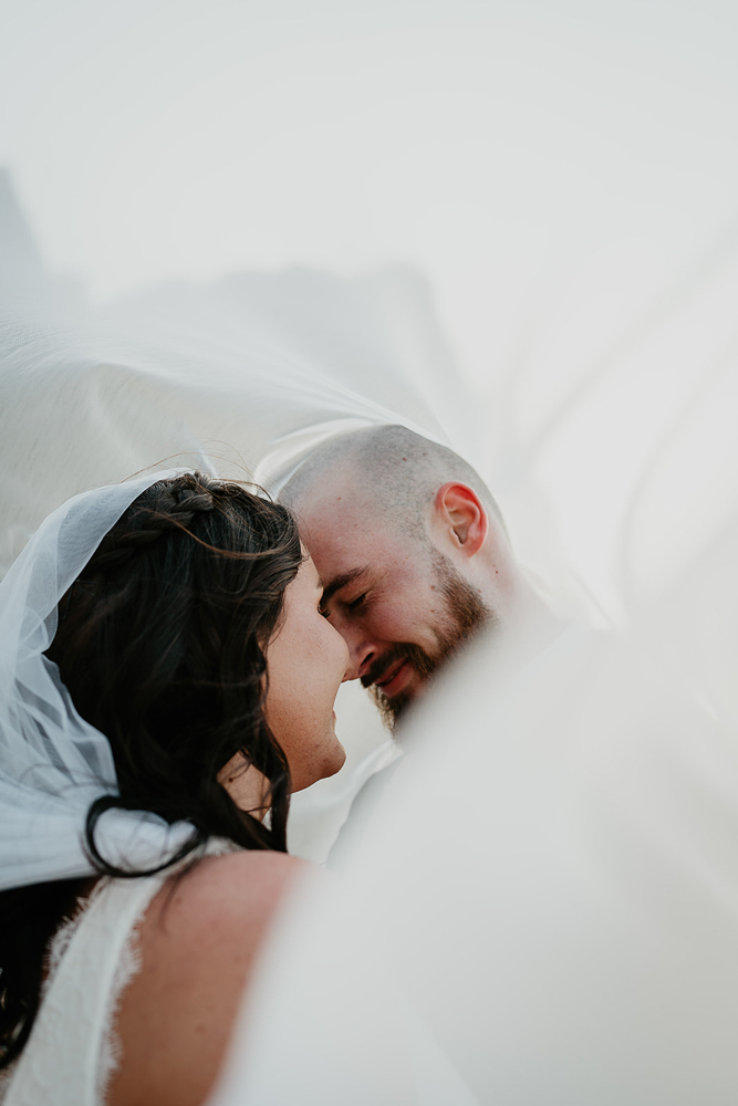 Newlyweds about to kiss with the bride's veil covering both of them.