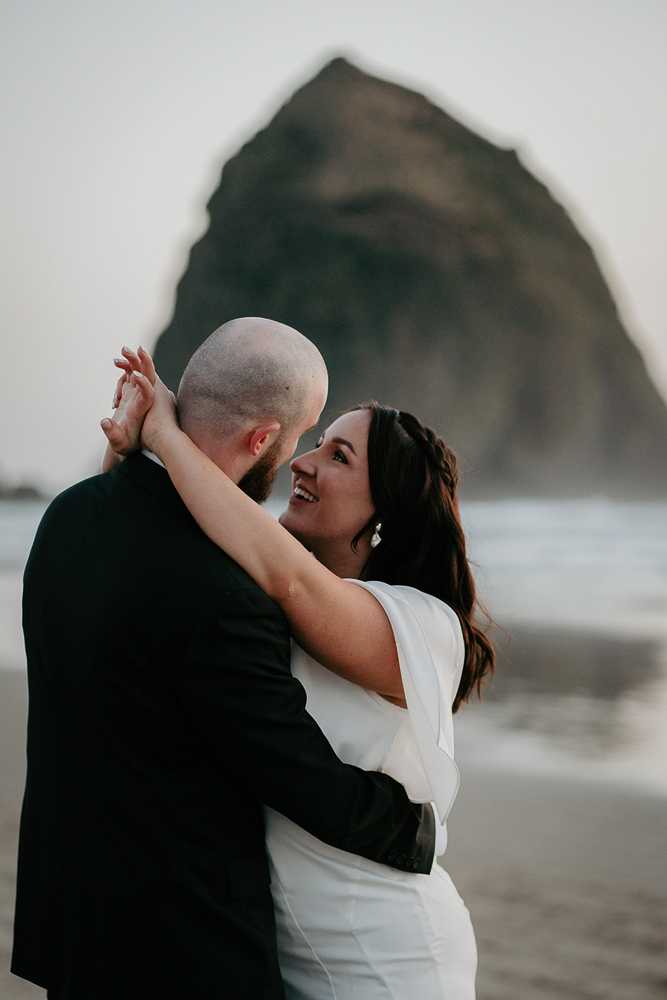 The bride and groom dancing on the sand with the sun setting and Haystack Rock in the background at Cannon Beach. 