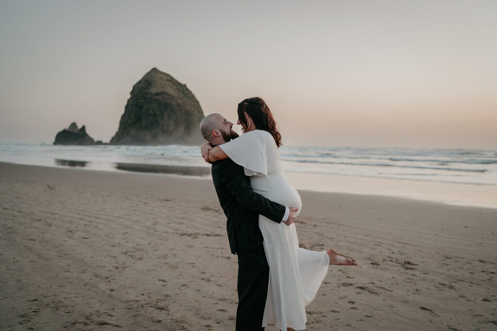 A bride and groom hugging at Cannon Beach in front of Haystack Rock as the sun sets.