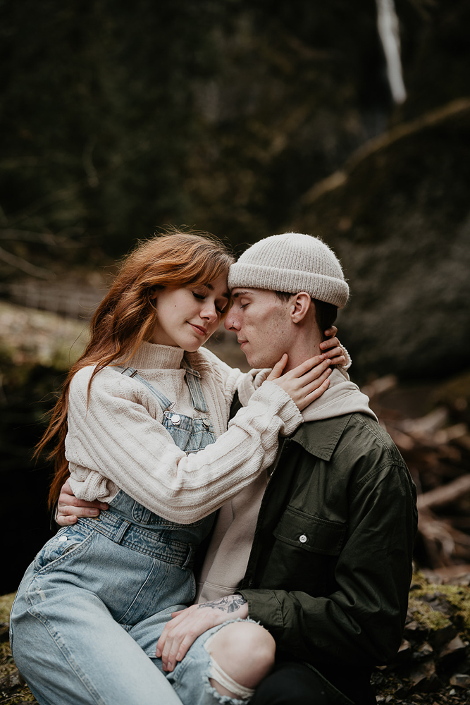 A couple hugging while sitting on a mossy log at the Columbia River Gorge. 