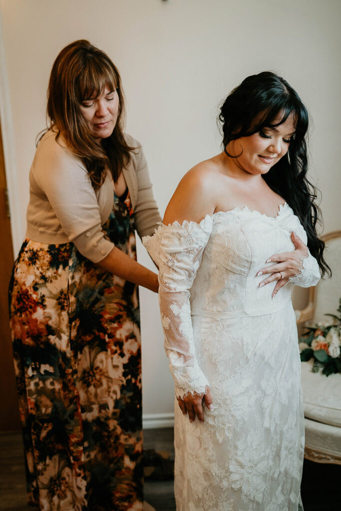 The bride getting her dress zipped up by her mom. 