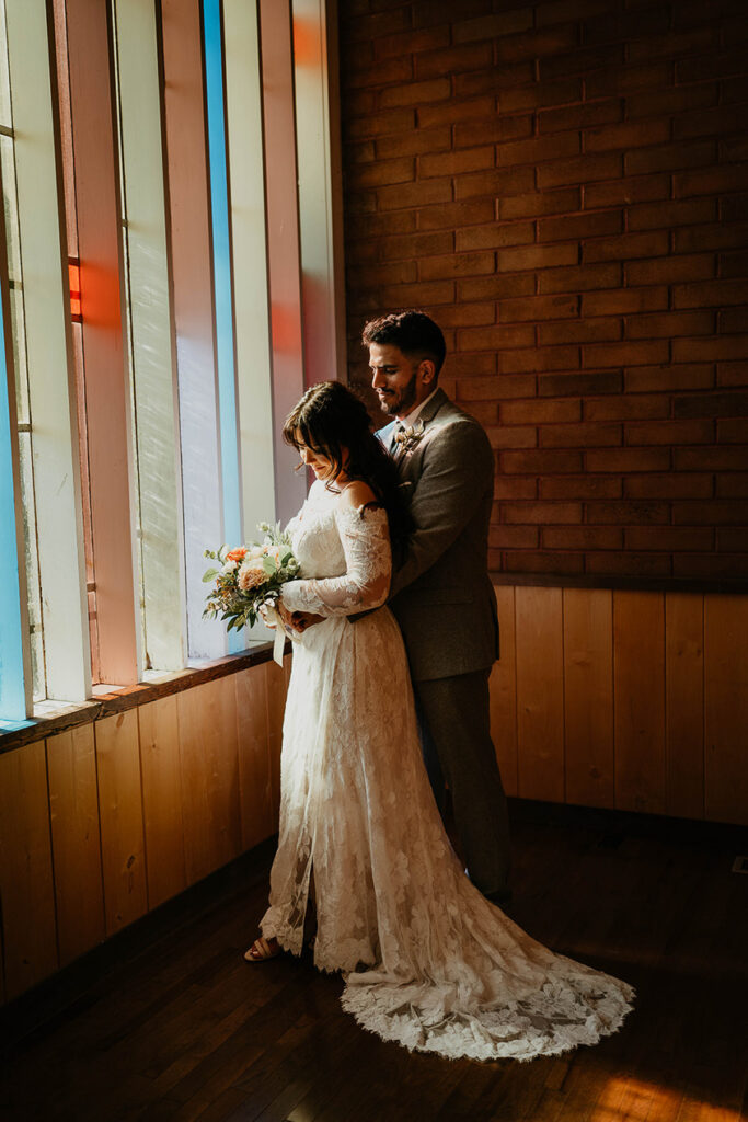 The bride and groom hugging, painted in light from the stained glass window. 