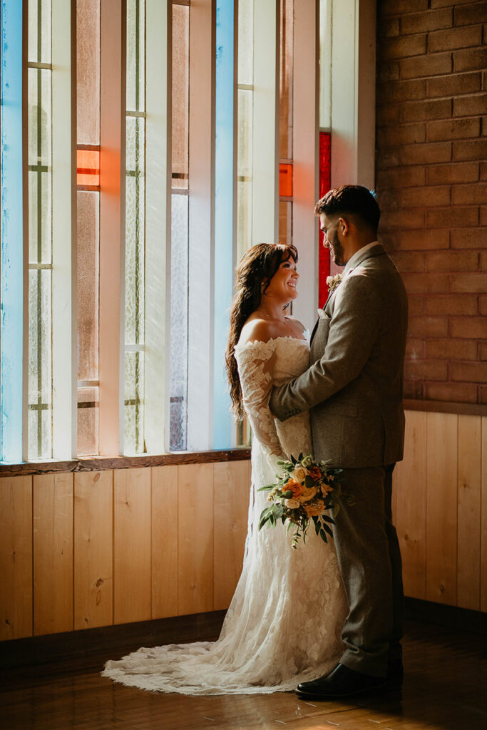 The bride and groom looking lovingly at each other, painted in light from the stained glass window. 