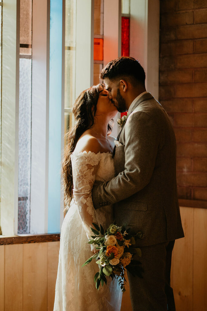 The bride and groom kissing, painted in light from the stained glass window. 