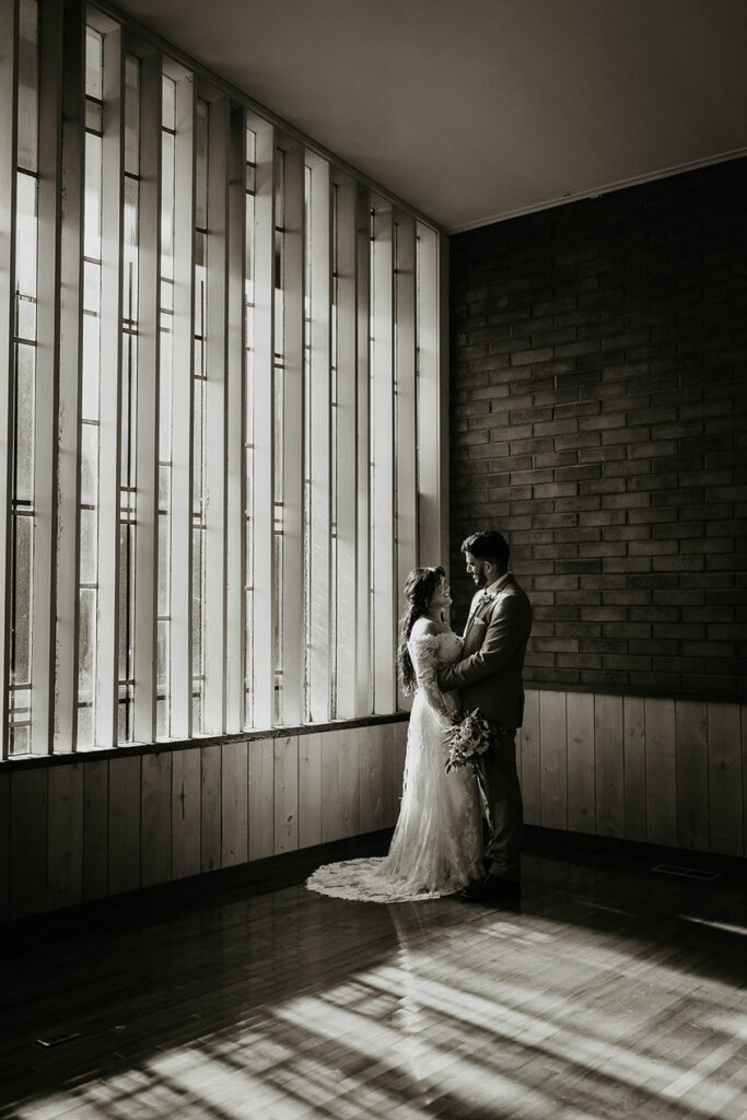 The bride and groom smiling at each other, painted in light from the stained glass window. 