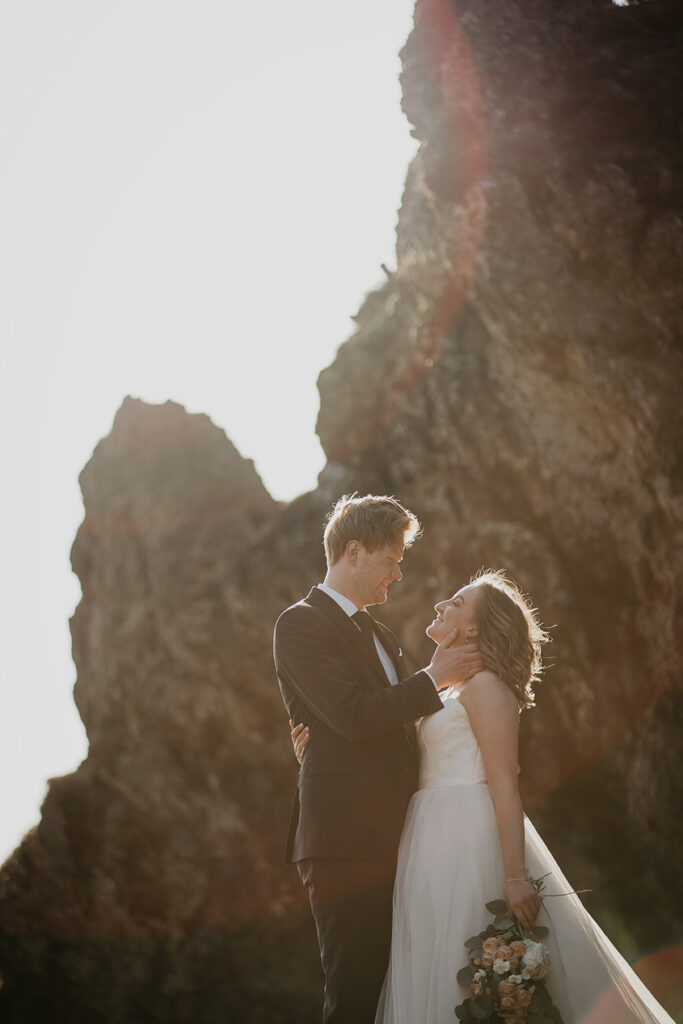 A couple staring lovingly into each other's eyes with large sea spires in the background. 