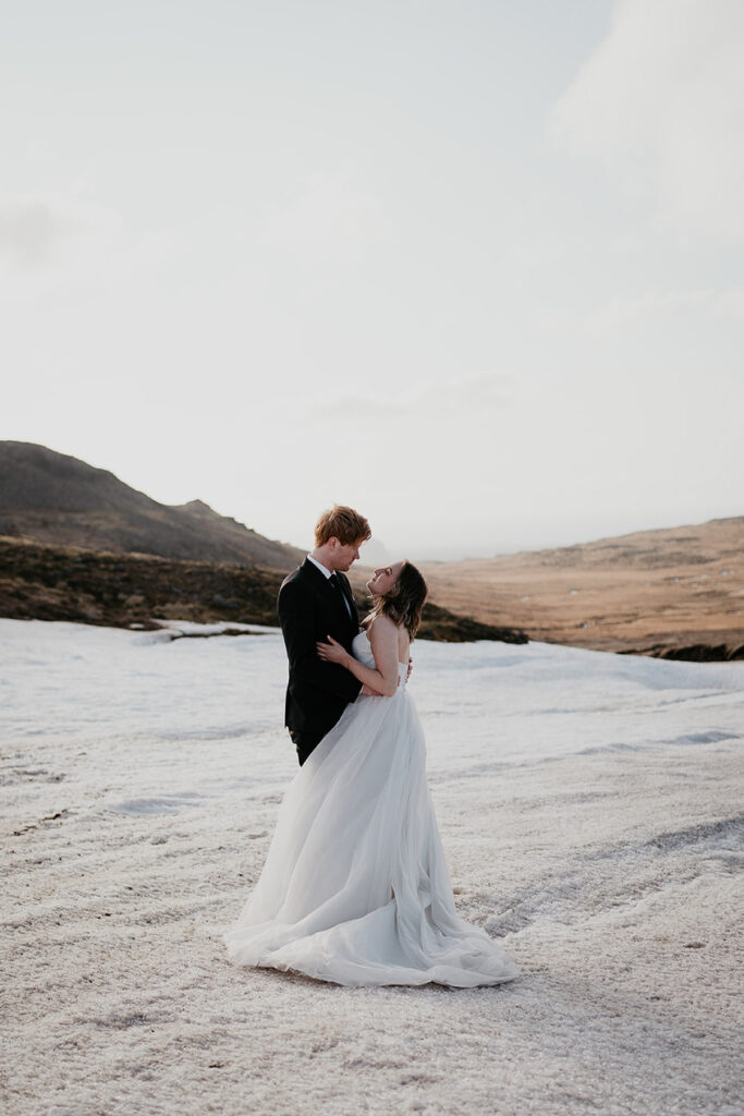 A bride and groom hugging while standing on a white sand beach. 