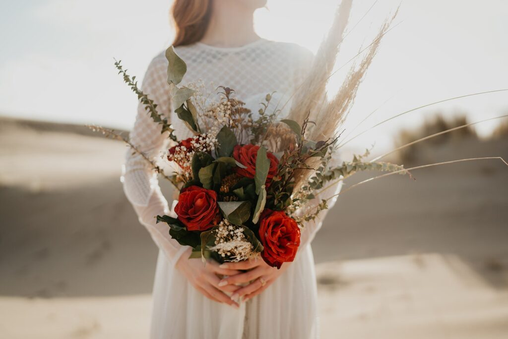 Bride holding orange, green, and beige elopement flowers during Oregon sand dunes elopement