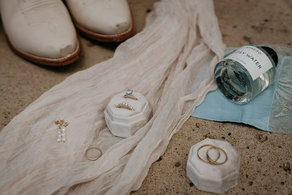 Rings, pearl earrings, boots, and water resting on sand. 