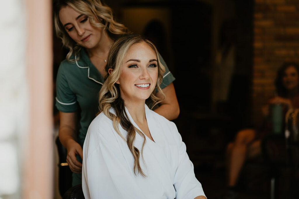 A bride smiling while her hair is getting done by a stylist. 