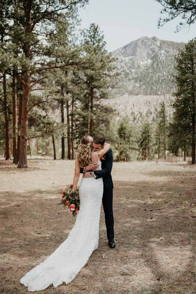 The bride and groom hugging in the forest, while the bride holds a bouquet of roses.