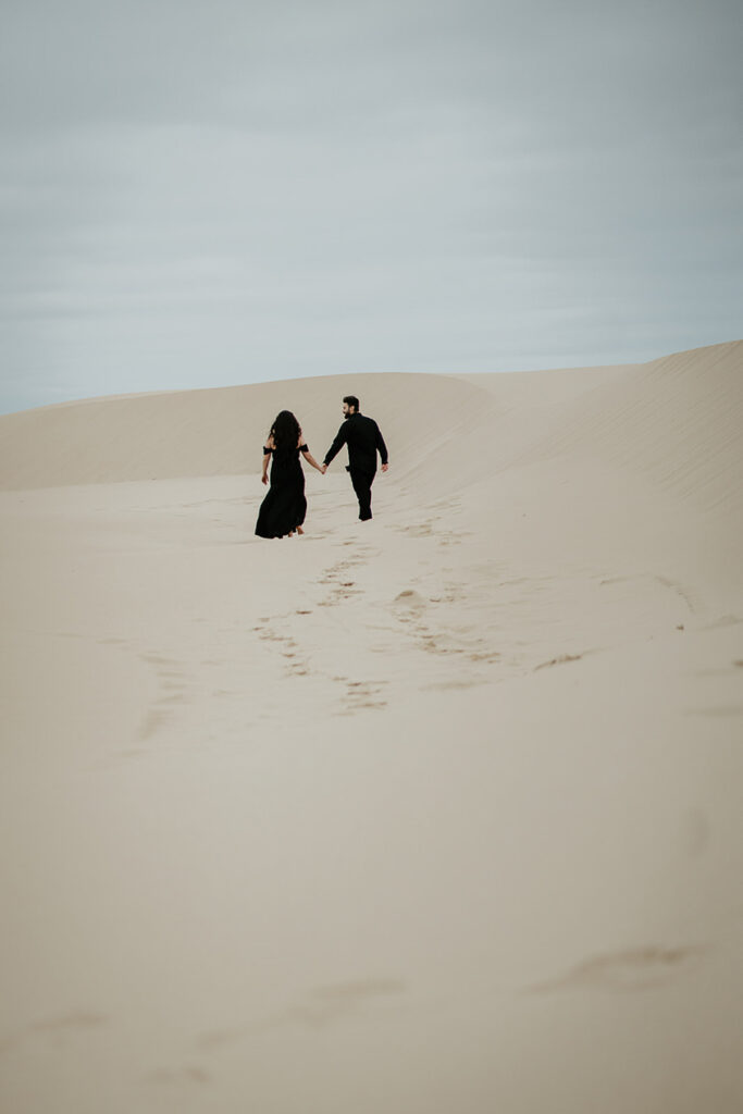 A couple holding hands while walking on the sand dunes in Oregon. 