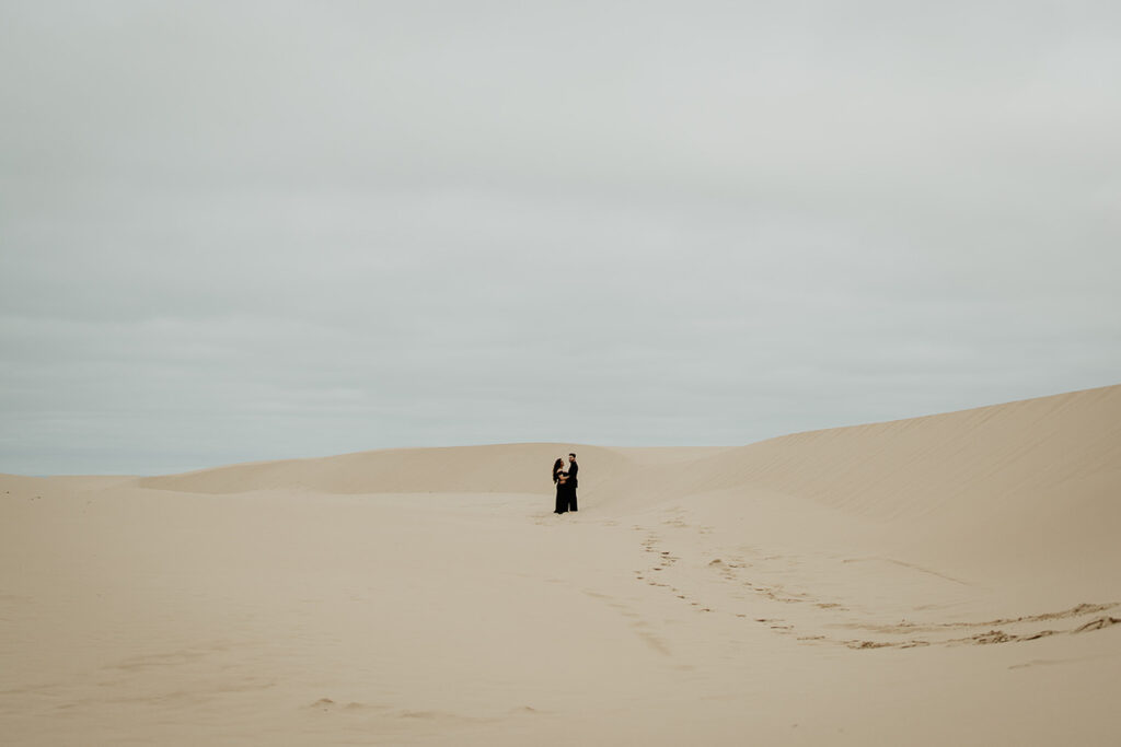 The Oregon Coast Sand Dunes with a couple holding hands in the middle of the picture. 