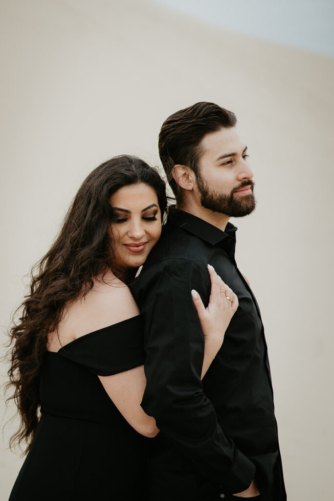 A fiance holding her boyfriend while standing on a sand dune in Oregon during their engagement shoot. 