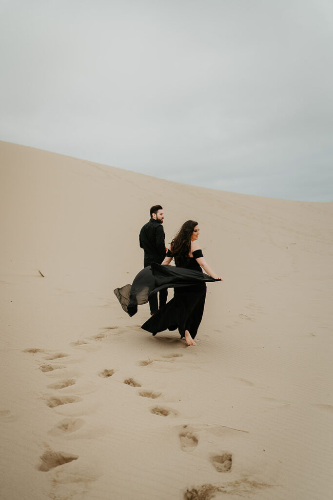 A couple walking, the girlfriend's dress flowing in the wind, walking on the Oregon sand dunes. 