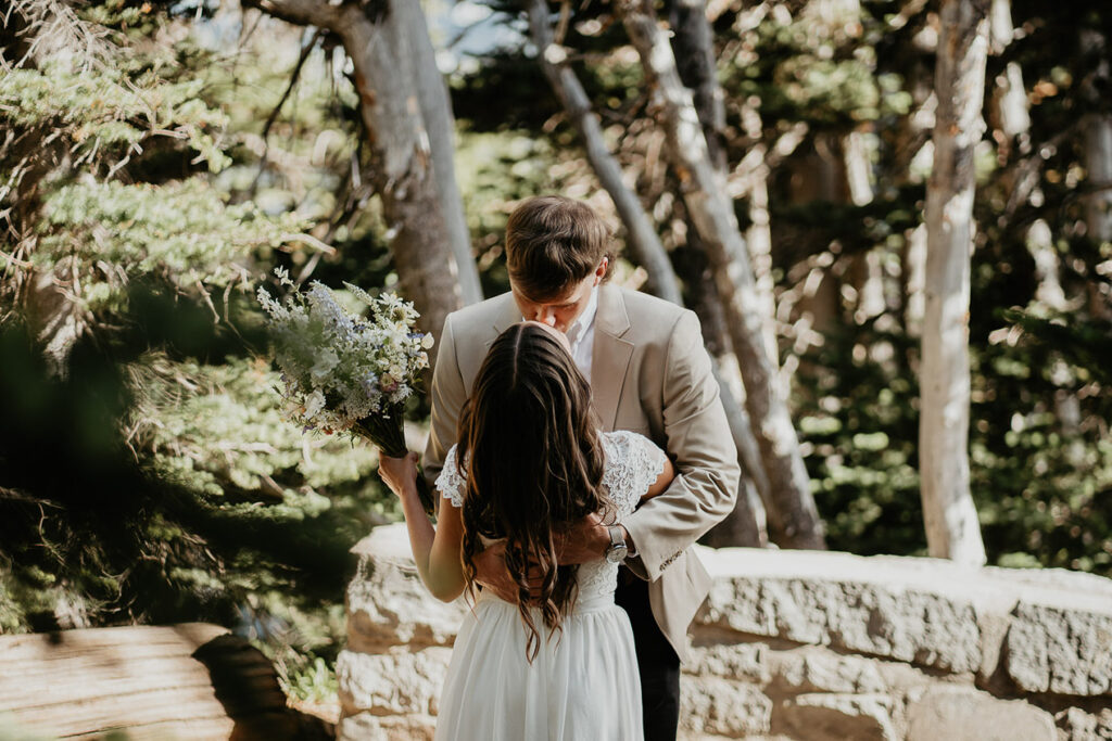 The couple kissing after their first look, with the bride holding a bouquet of flowers. 