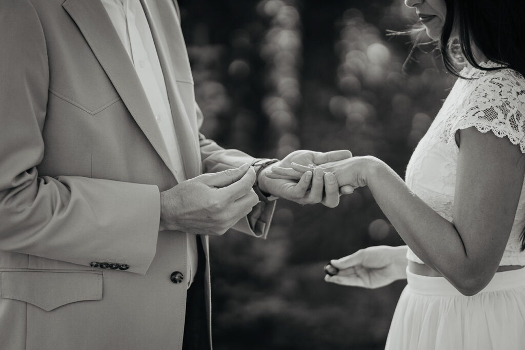 A black and white photo of the husband putting on her bride's ring. 