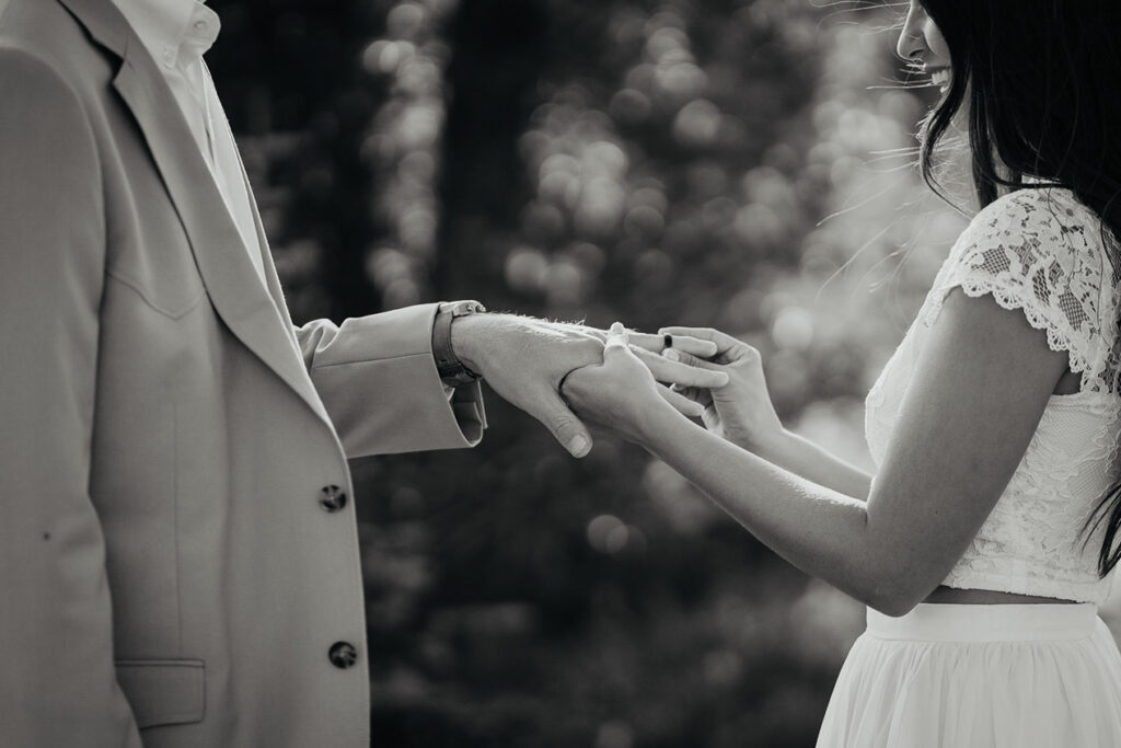 A black and white photo of the bride putting on her husband's ring. 