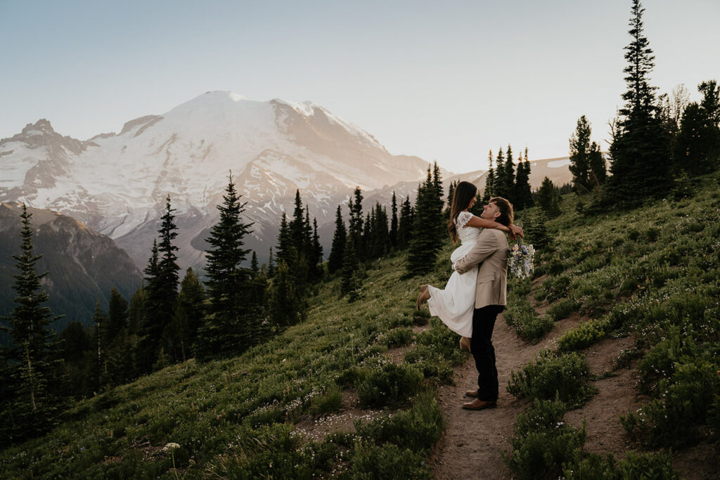 The groom picking up his wife with Mt Rainier in the background during their elopement.