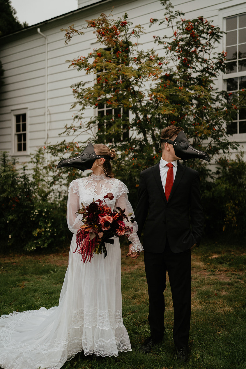 A couple wearing bird masks holding hands in front of a chapel. 