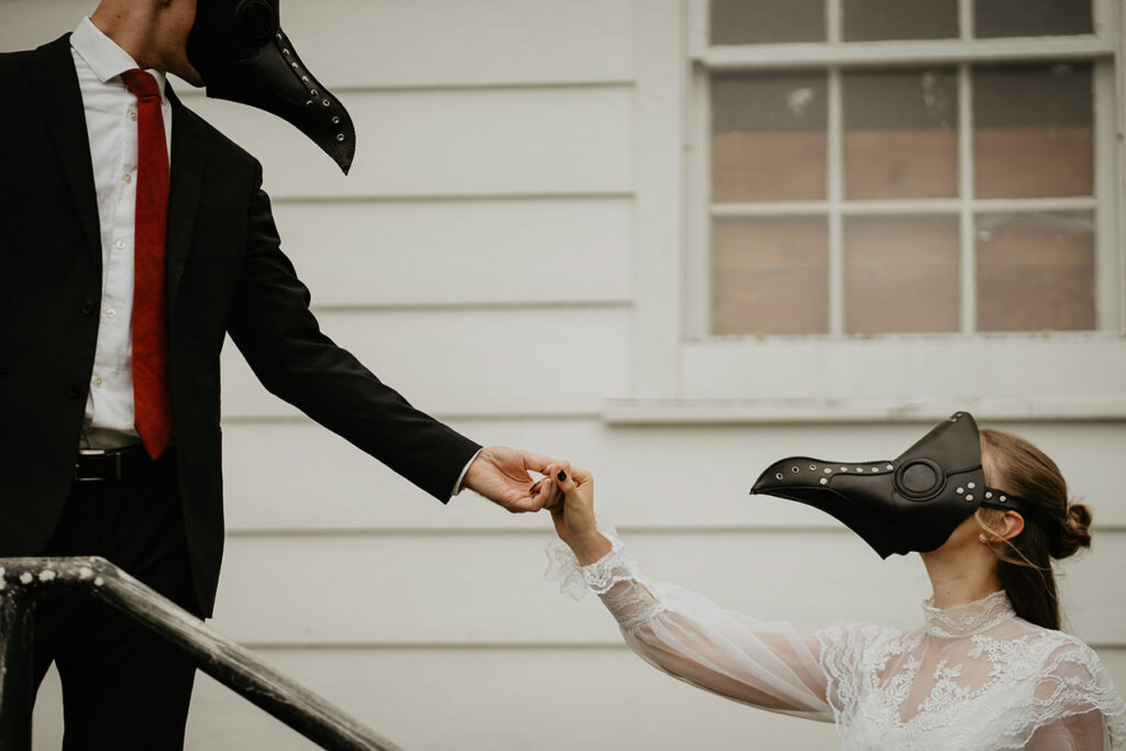 The husband leading his wife up the stairs of a chapel. They both are wearing bird masks. 