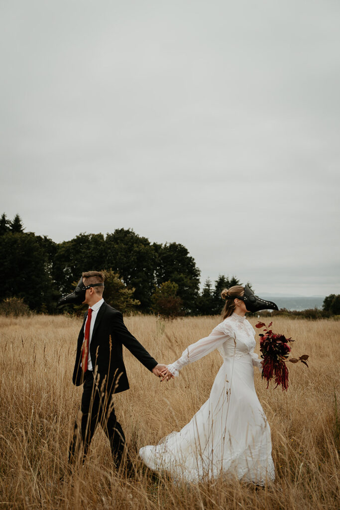 A couple wearing bird masks walking away from each other in an open field. 