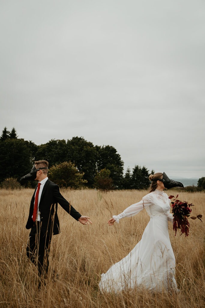 A couple wearing bird masks walking away from each other in an open field. 