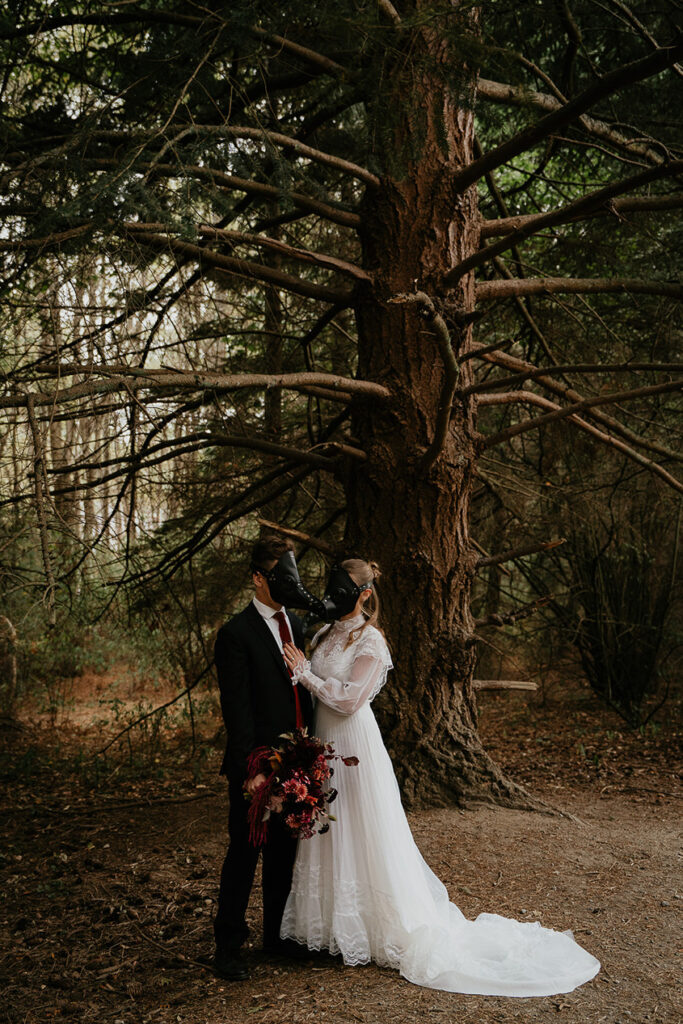 A couple wearing bird masks holding each other in the forest. 