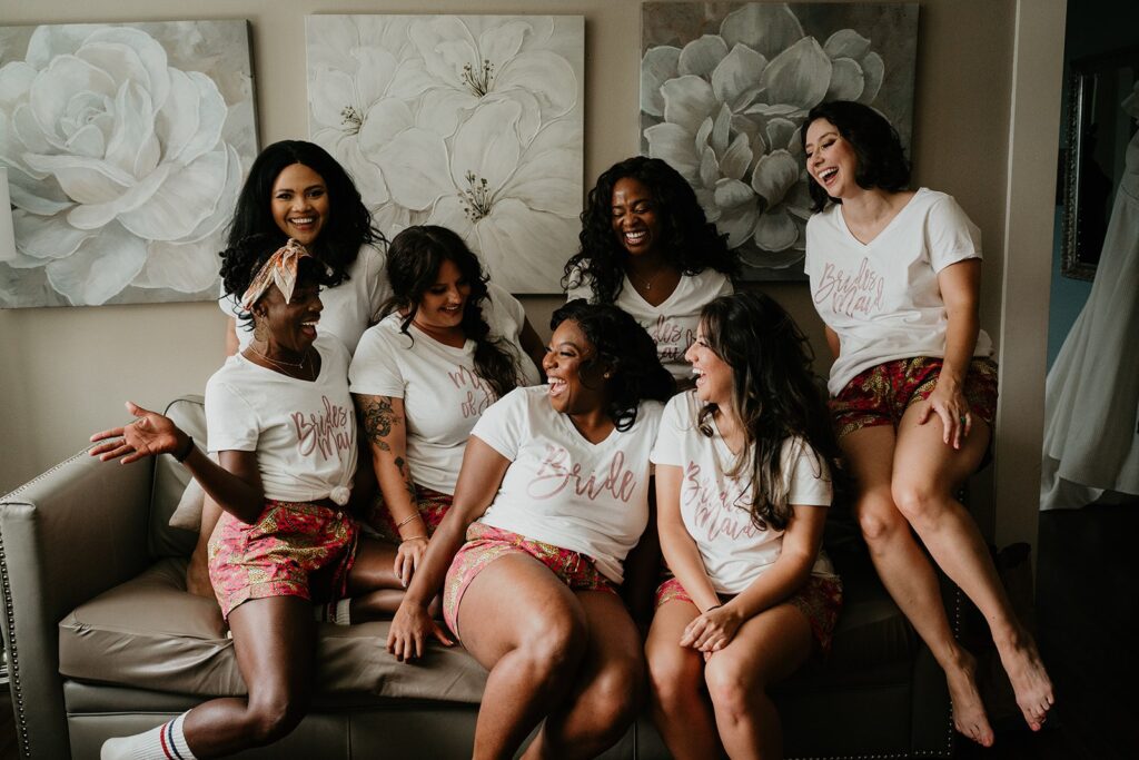 Bride sitting on a couch laughing with bridesmaids