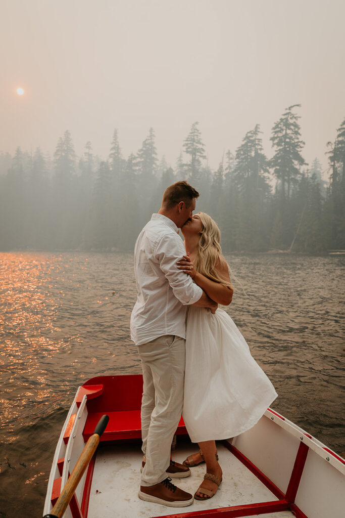 A couple standing in a row boat on Lost Lake, with smoke and pine trees in the background.