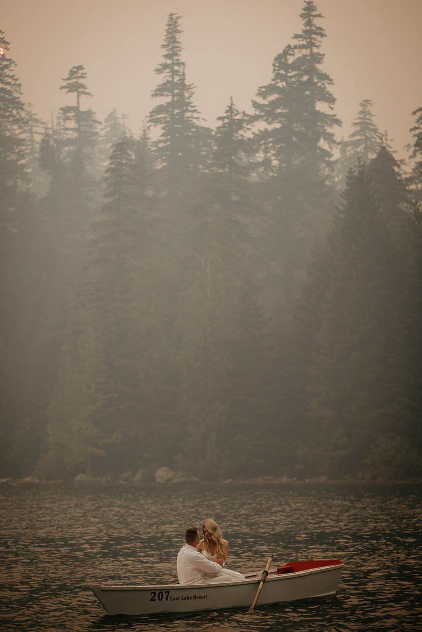 A couple holding each other in a row boat while smoke fills the air. 