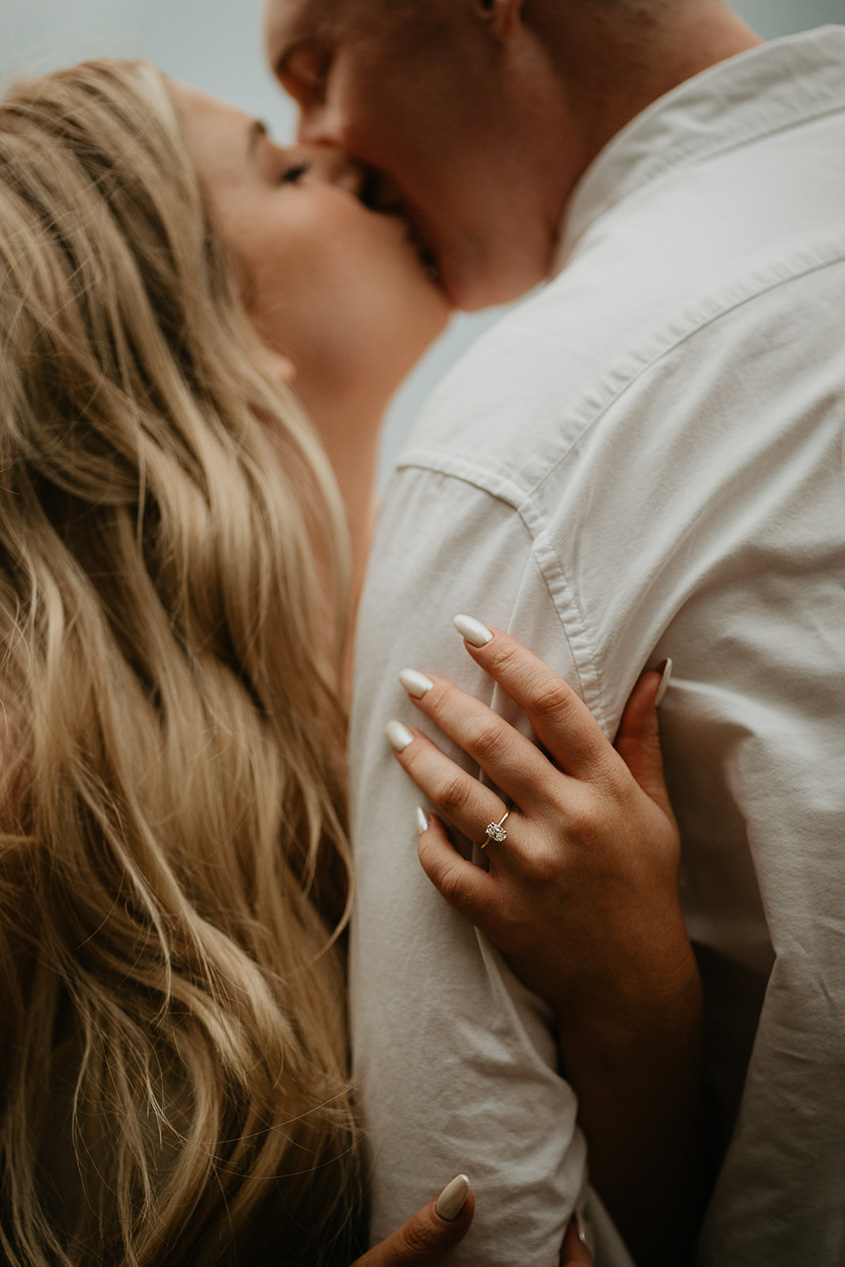 The couple kissing, with the future bride showing off her engagement ring. 