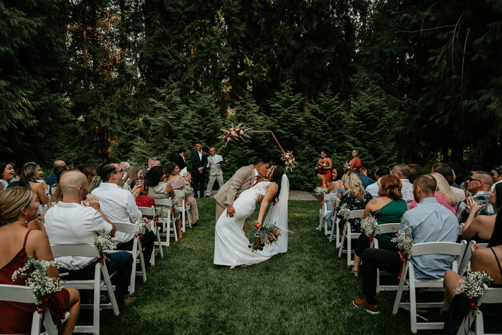 The couple kissing in front of their wedding attendees.