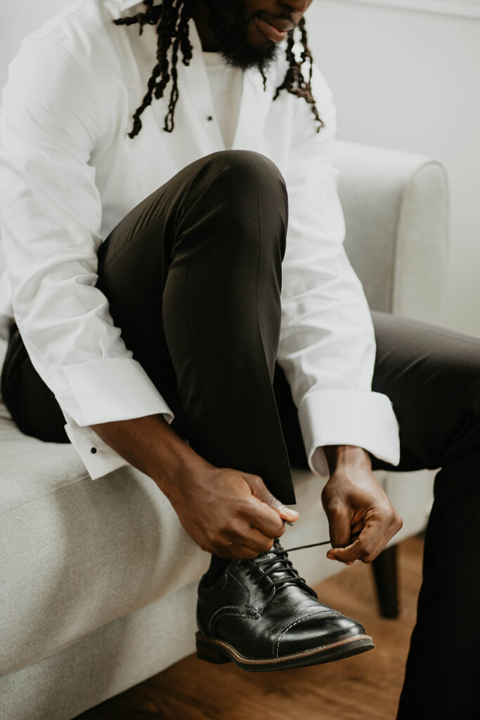 the groom getting ready and tying his shoe. 