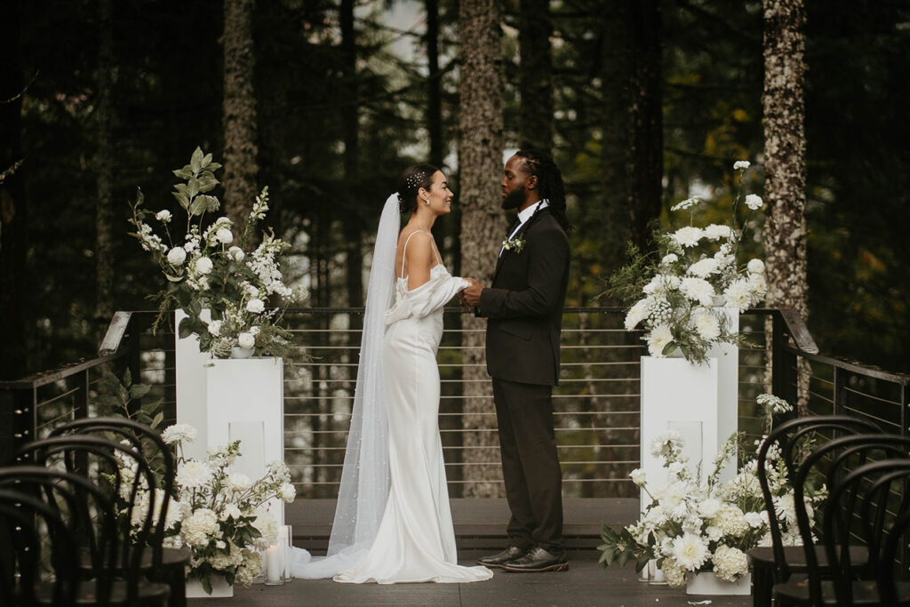 The bride and groom standing at Rocky Hill Weddings & Events' altar, with white flowers on either side of them.