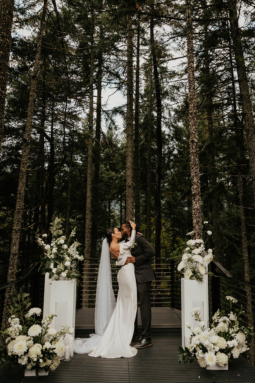 The bride and groom kissing at Rocky Hill Weddings & Events' altar, with white flowers on either side of them.