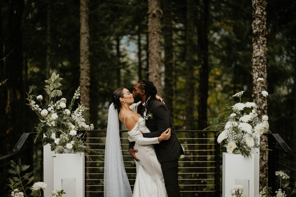 The bride and groom kissing at Rocky Hill Weddings & Events' altar, with white flowers on either side of them.